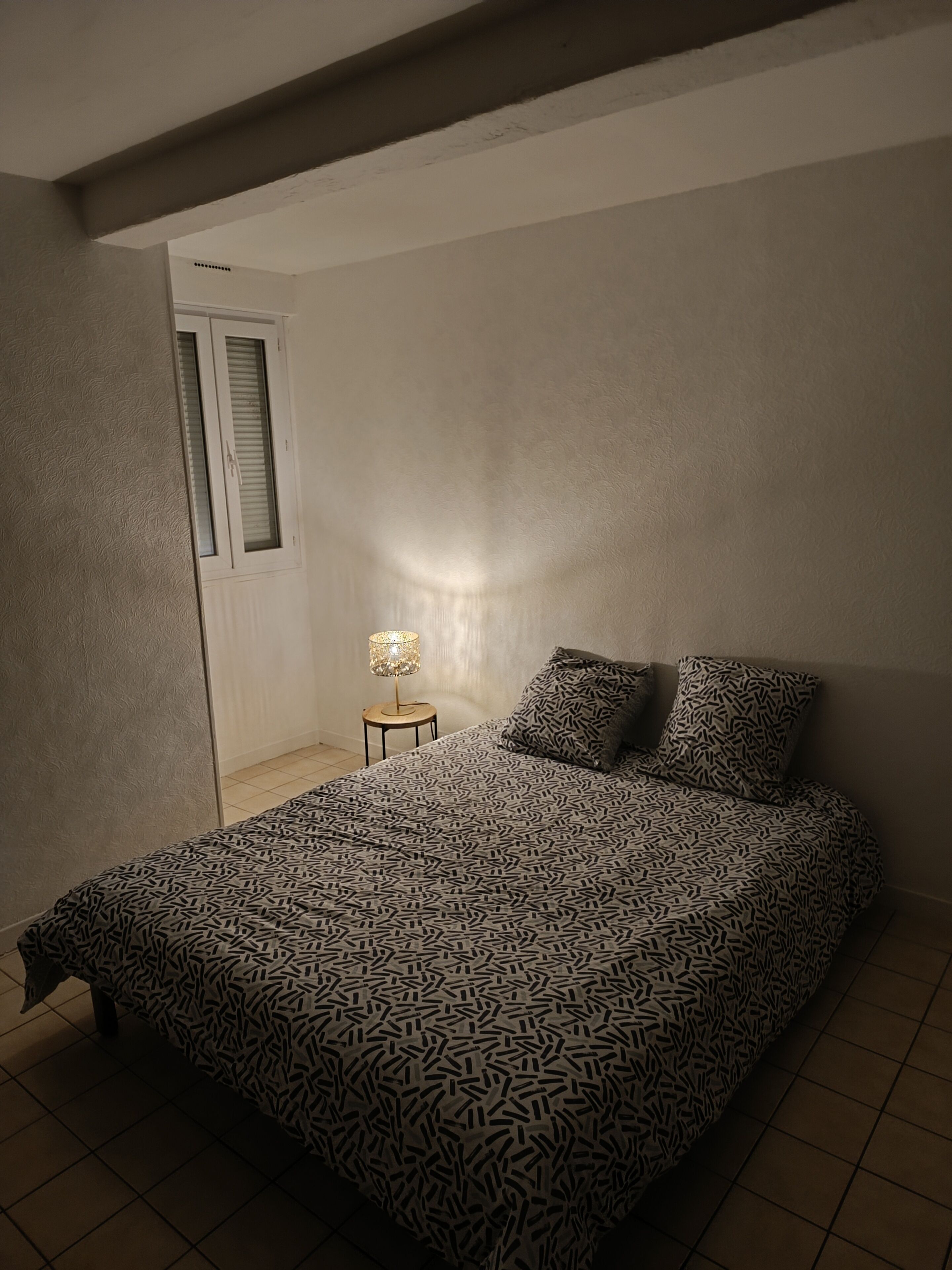 Une chambre à coucher avec une couvre-lit à motifs, une lampe de chevet et une porte équipée de stores.