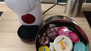 Eine Küchenarbeitsplatte mit einer Nescafé Dolce Gusto Kaffeemaschine, einem Edelstahlbehälter voller verschiedener Kaffeekapseln und einem Metall-Utensilienhalter.