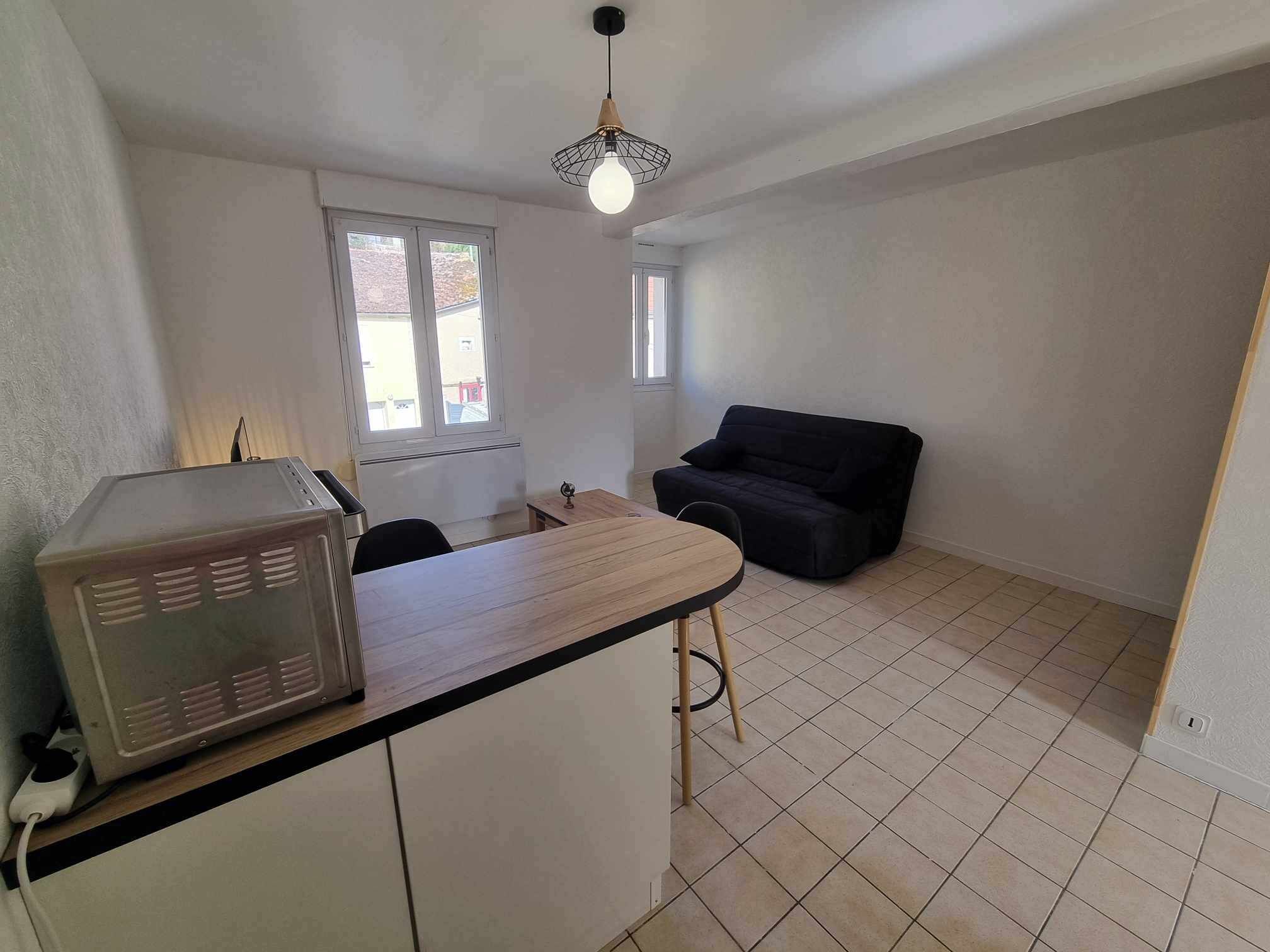 Eine kompakte Küche mit Mikrowelle, einem kleinen Tisch und einem schwarzen Sofa. Ein Fenster sorgt für natürliches Licht, und eine Deckenleuchte ist installiert.