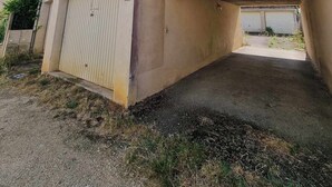 Un immeuble de deux étages avec une façade beige, une porte de garage blanche et un petit jardin à l’avant.
