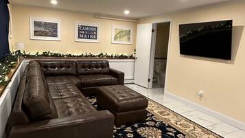A living room with a sectional sofa, a large flat-screen TV, and a decorative rug.