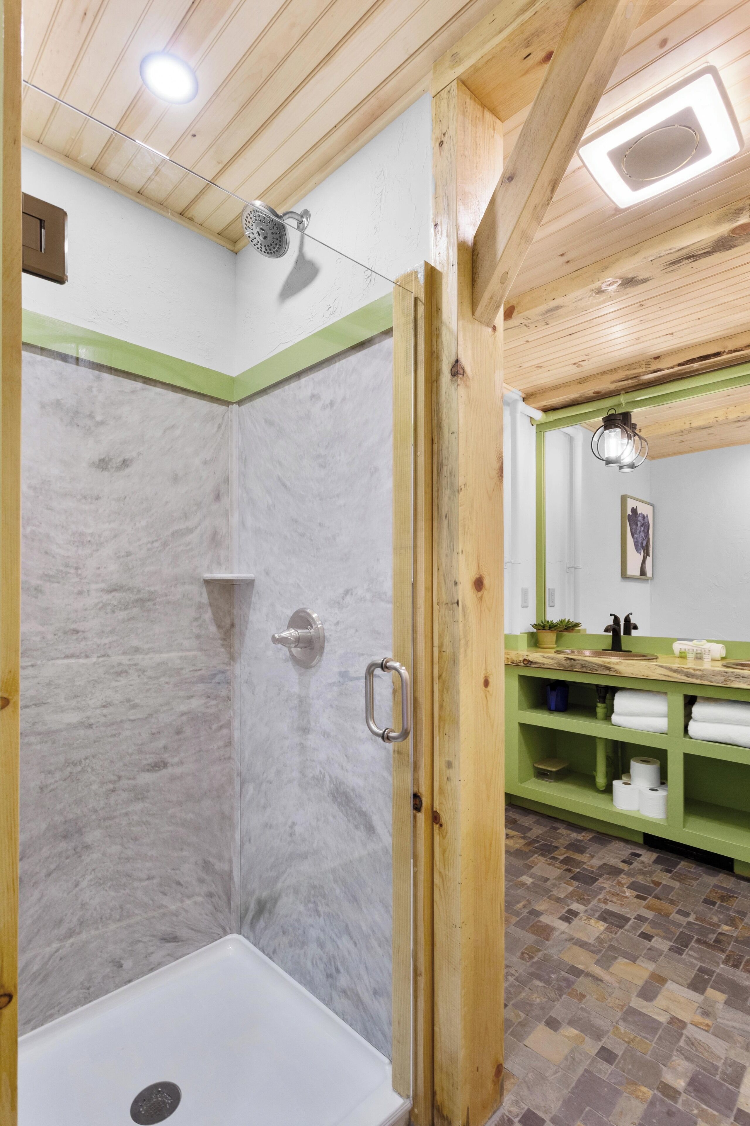 A shower area with a glass door, a wooden ceiling, and a green accent wall.