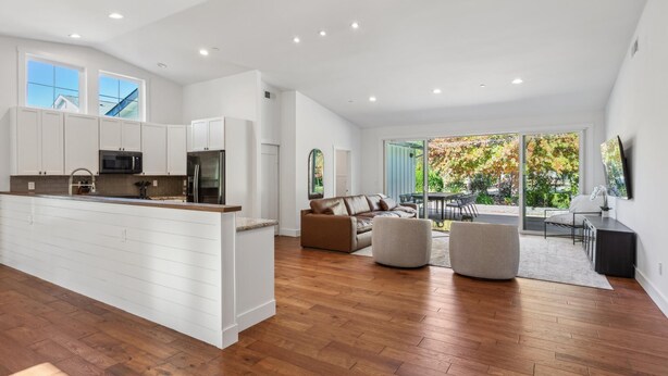 A modern kitchen with white cabinetry, a central island, and a dining area with a brown leather sofa and ottoman.