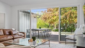 A modern living room with a glass coffee table, leather sofa, and a dining area with a table and chairs.