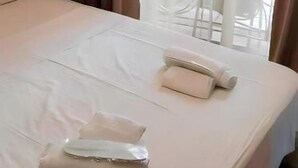 Habitación de hotel con cama, dos almohadas, una toalla doblada y una ventana con cortinas.