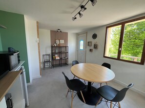 Un coin repas avec une table ronde et quatre chaises, une bibliothèque, un four à micro-ondes et une vue sur la verdure par la fenêtre.