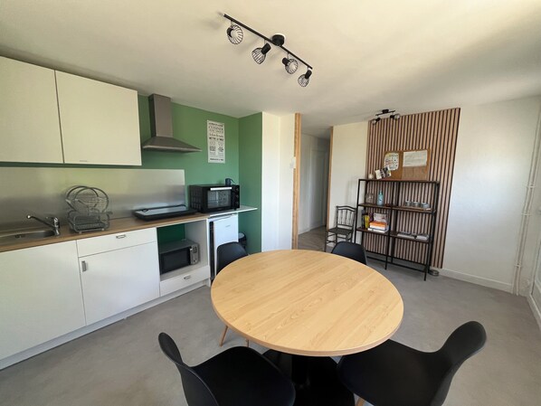 Cocina compacta con microondas, tostadora y lavabo. En primer plano, una mesa de comedor con sillas.