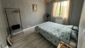 Un dormitorio con cama, ventilador, lámpara colgante y ventana con cortinas.