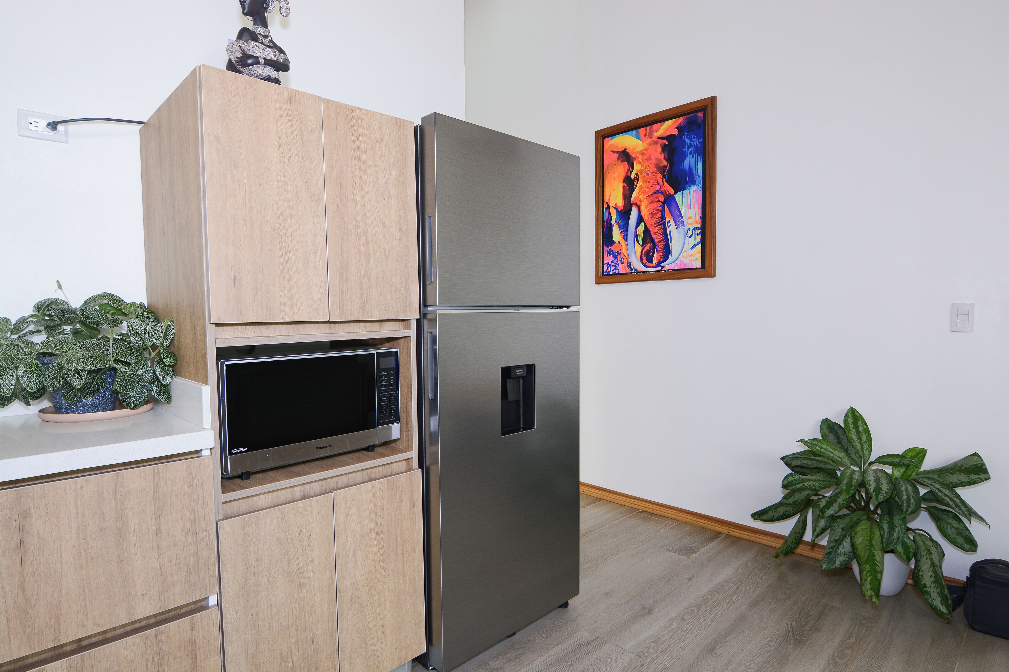 Une cuisine moderne équipée d’un réfrigérateur en acier inoxydable, de meubles en bois, d’un four à micro-ondes et de deux plantes en pot.