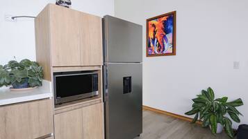Une cuisine moderne équipée d’un réfrigérateur en acier inoxydable, de meubles en bois, d’un four à micro-ondes et de deux plantes en pot.