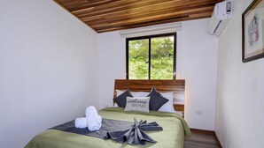 A neatly made bed with a green bedspread, a welcome home pillow, and towels on the side. - Nambi Monteverde (Monteverde)
