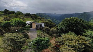 A modern house with a large glass door, surrounded by lush greenery and hills in the background. - Nambi Monteverde (Monteverde)