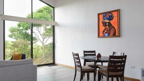 A modern dining area with a wooden ceiling, a large window with a view of trees, and a painting on the wall. - Nambi Monteverde (Monteverde)