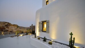 A modern building with a white exterior, a small window with open shutters, and a well-lit exterior wall. - Coastal Retreat With Wellness (Mykonos)