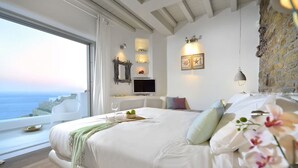 A modern bedroom with a large bed, a TV, and a view of the sea. - Coastal Retreat With Wellness (Mykonos)