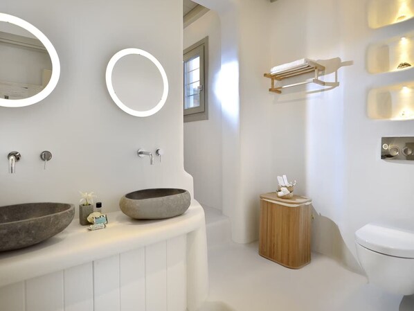 A modern bathroom with two sinks, a large mirror, a wooden stool, and a toilet.