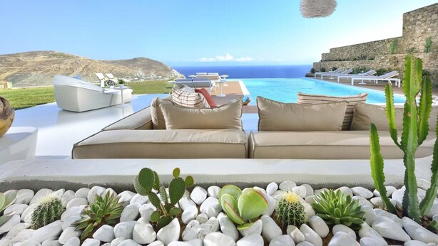A poolside lounge with a view of the sea, surrounded by cacti and rocks. - Coastal Retreat With Wellness (Mykonos)