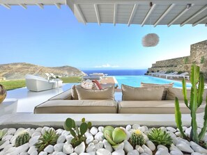 A poolside lounge with a view of the sea, surrounded by cacti and rocks. - Coastal Retreat With Wellness (Mykonos)