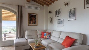 A living room with a sofa, a coffee table with books, a window with curtains, and framed pictures on the wall.