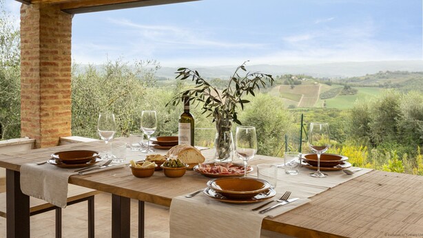 A dining table set outdoors with a view of rolling hills and vineyards.