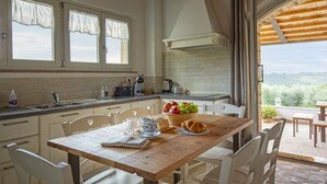 A kitchen with a wooden table set for breakfast, a view of the countryside, and a large window with curtains.