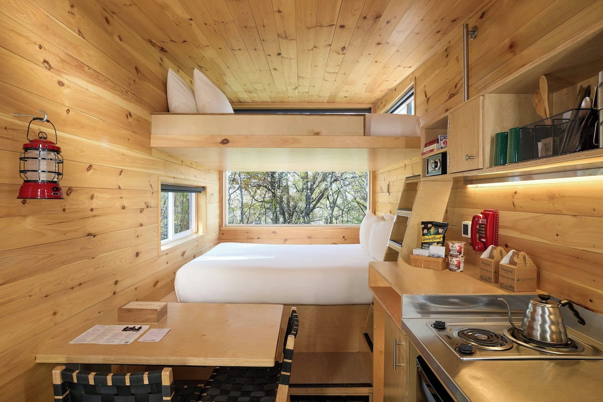 A compact wooden cabin with a bunk bed, a kitchenette, and a small dining area.