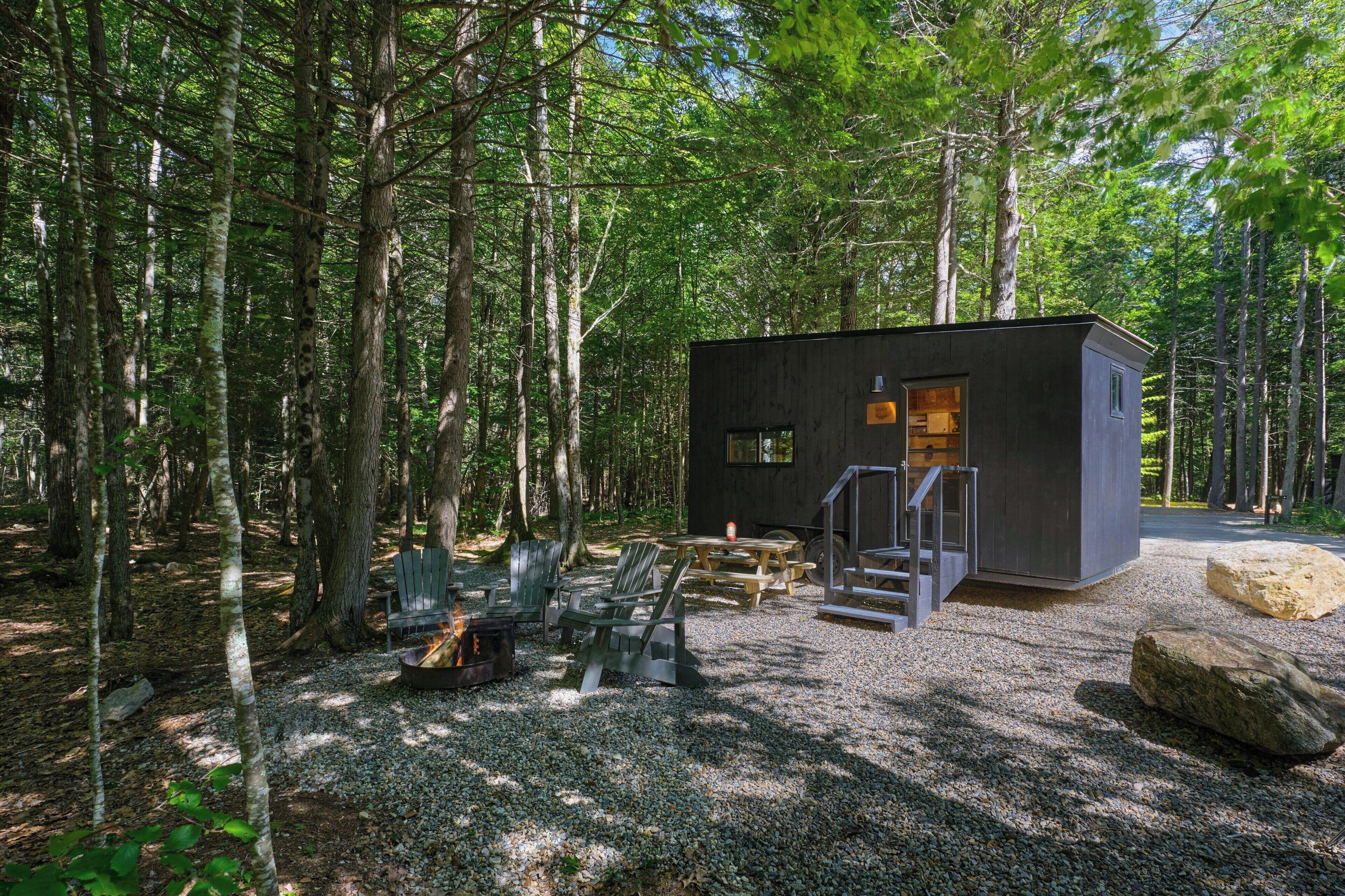 A cabin with a gravel ground, wooden deck, and a fire pit.
