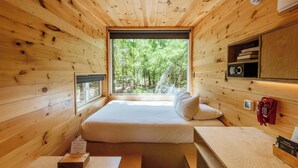 A wooden cabin room with a bed, a desk, and a window offering a forest view. - Postcard Cabins Brown County Indiana, Outdoor Collection by Marriott Bonvoy (Columbus)