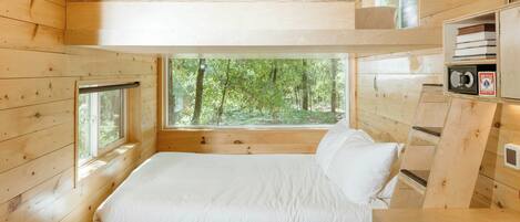 Een slaapkamer in een houten hutje, met een stapelbed, grote ramen en ingebouwde opbergruimte.