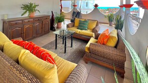 Eine sonnendurchflutete Terrasse mit Korbmöbeln, einem Glastisch und Topfpflanzen.
