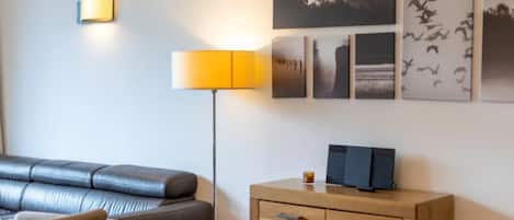 Une chambre d’hôtel moderne avec un canapé en cuir, une table d’appoint en bois, une lampe et des tableaux encadrés au mur.