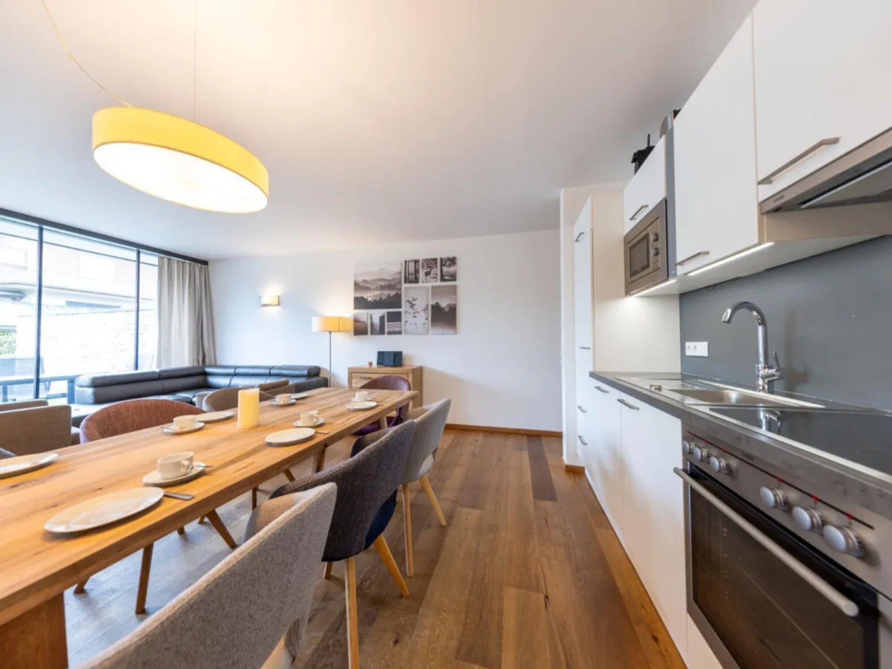 Una cocina moderna con electrodomésticos de acero inoxidable, un comedor con mesa y sillas de madera, y una sala de estar con sofá y lámpara.