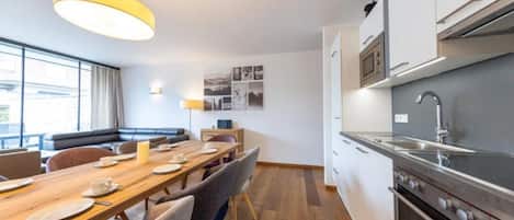 Una cocina moderna con electrodomésticos de acero inoxidable, un comedor con mesa y sillas de madera, y una sala de estar con sofá y lámpara.