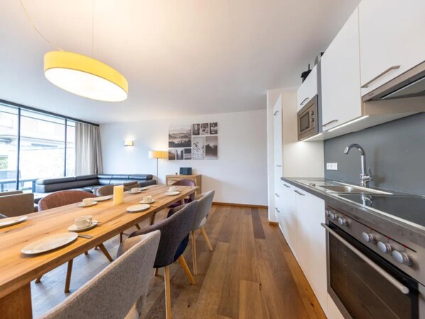 Une cuisine moderne équipée d’appareils électroménagers en acier inoxydable, un coin repas avec une table et des chaises en bois, et un espace détente avec un canapé et une lampe.