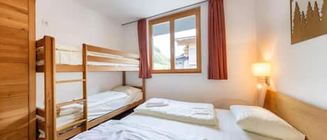 A room with bunk beds, a window with curtains, a wall-mounted lamp, and a painting.
