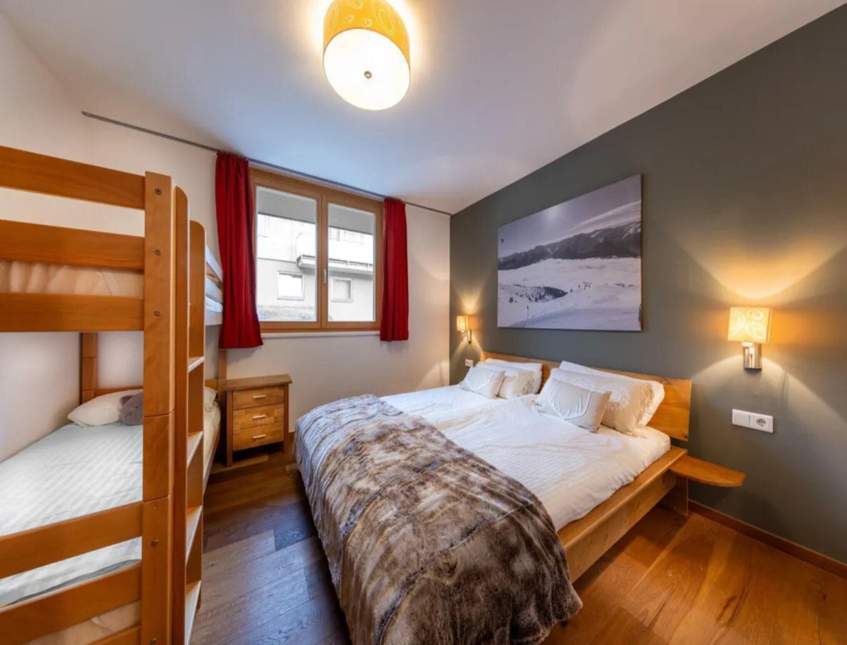 Un dormitorio con literas, una cama individual, una mesita de noche, una lámpara, un cuadro y una ventana con cortinas.