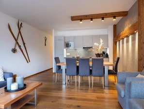 Un salon moderne avec une table à manger en bois, des canapés gris et une cuisine en arrière-plan.