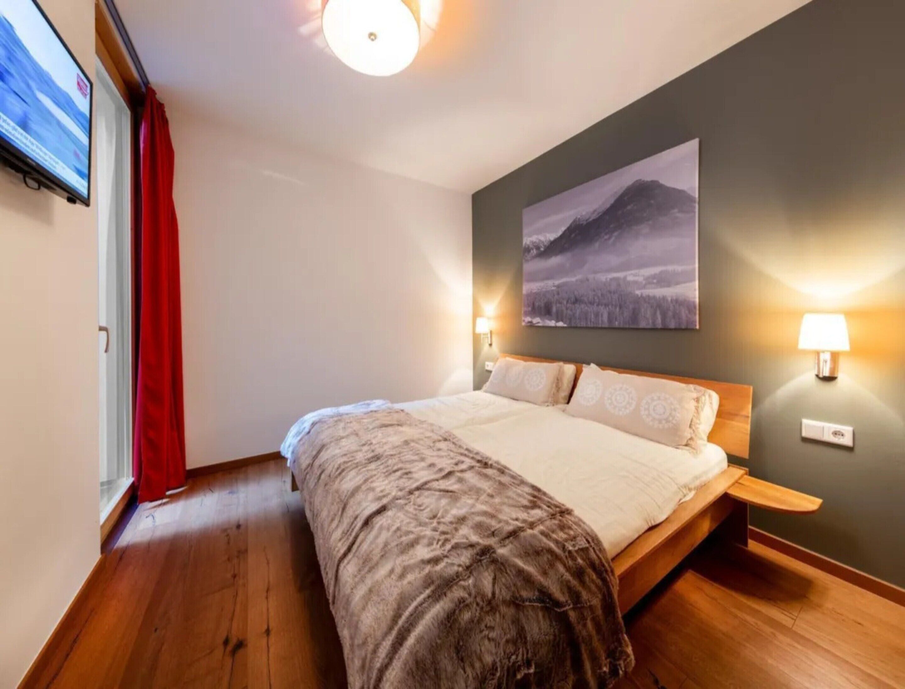 A bedroom with a bed, a mounted TV, two bedside lamps, and a wall-mounted picture.