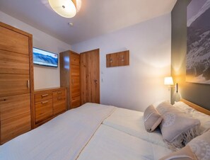 Un dormitorio con cama, armario de madera, televisor y lámpara de pared.