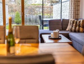 A modern living room with a sofa, a coffee table, and a view of a garden through large windows. - Sunlit Alpine Apartment in Neukirchen (Neukirchen am Grossvenediger)
