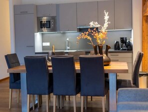 A modern kitchen with a dining table, chairs, and a vase with flowers. - Sunlit Alpine Apartment in Neukirchen (Neukirchen am Grossvenediger)