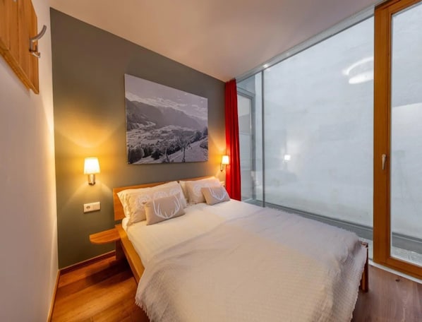 Une chambre à coucher avec un lit, une table de chevet, une lampe fixée au mur, une fenêtre donnant sur un beau paysage et un tableau accroché au mur.