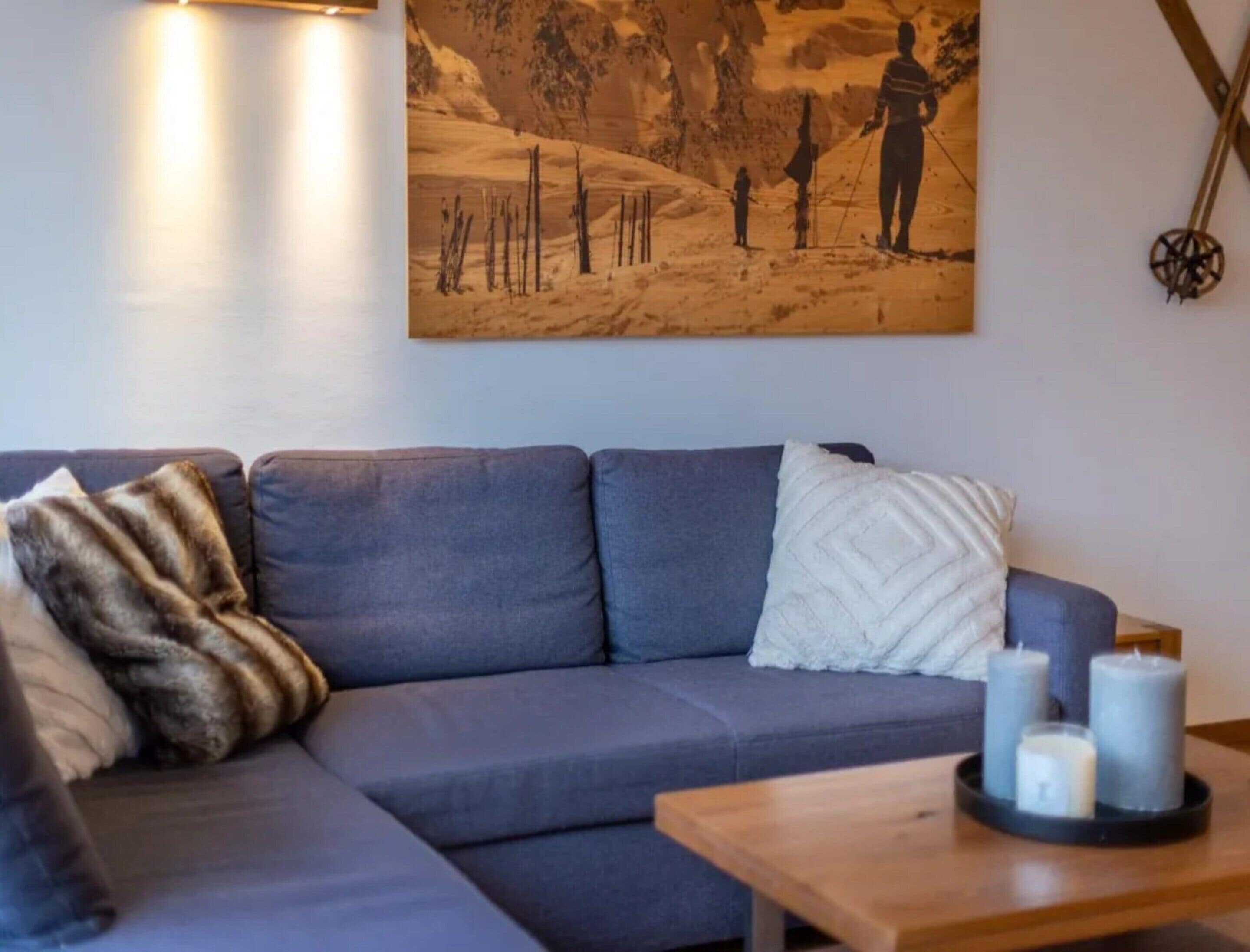 Una sala de estar con un sofá gris, un cojín blanco y una mesa de centro de madera con velas.