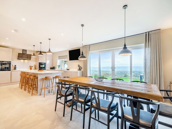 A modern kitchen with a large island, bar stools, and a dining area with a view. - Cherry Tree Cottage - UK47756 (Mellor)