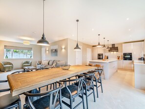 A modern kitchen with a central island, pendant lighting, and a dining area with a wooden table and chairs. - Cherry Tree Cottage - UK47756 (Mellor)
