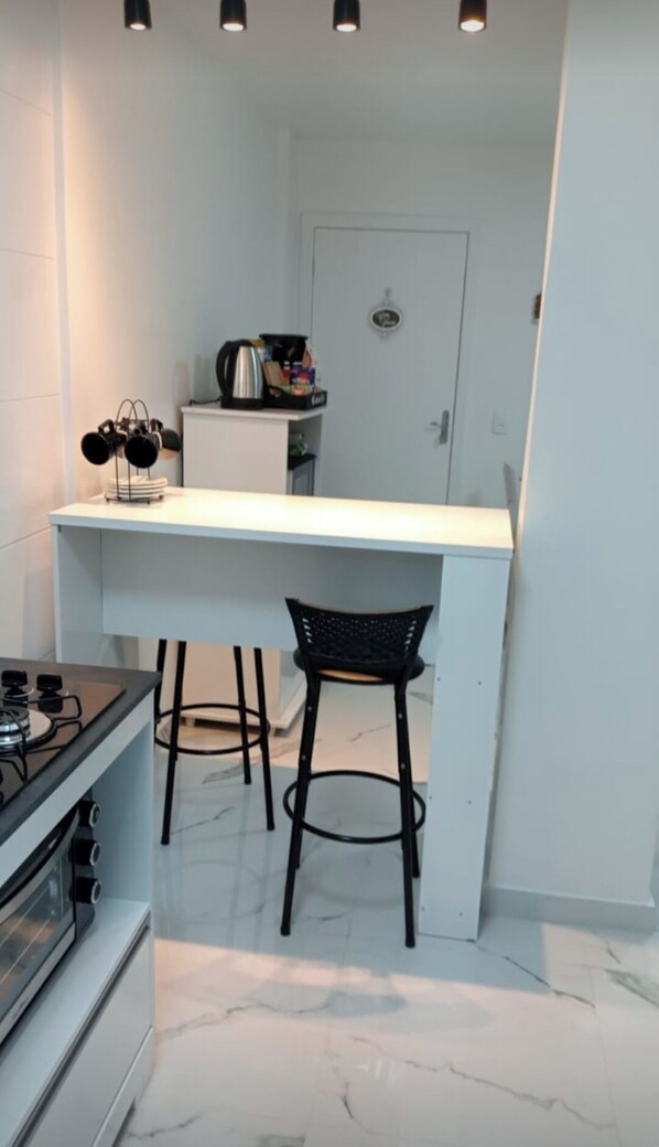 A compact kitchen with a white countertop, two black stools, and a coffee machine.