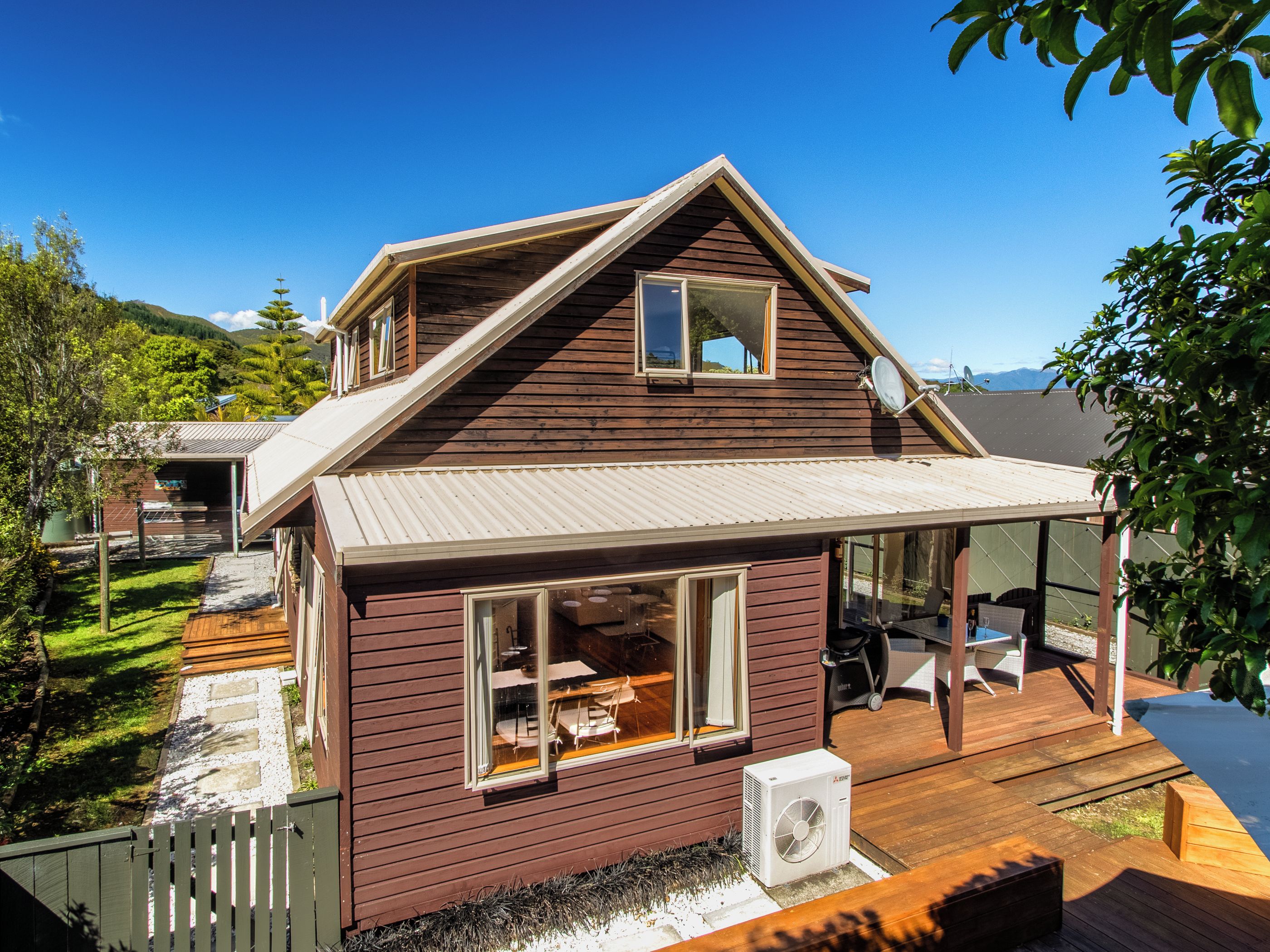 A wooden house with a covered porch, a satellite dish, and a view of a green landscape.