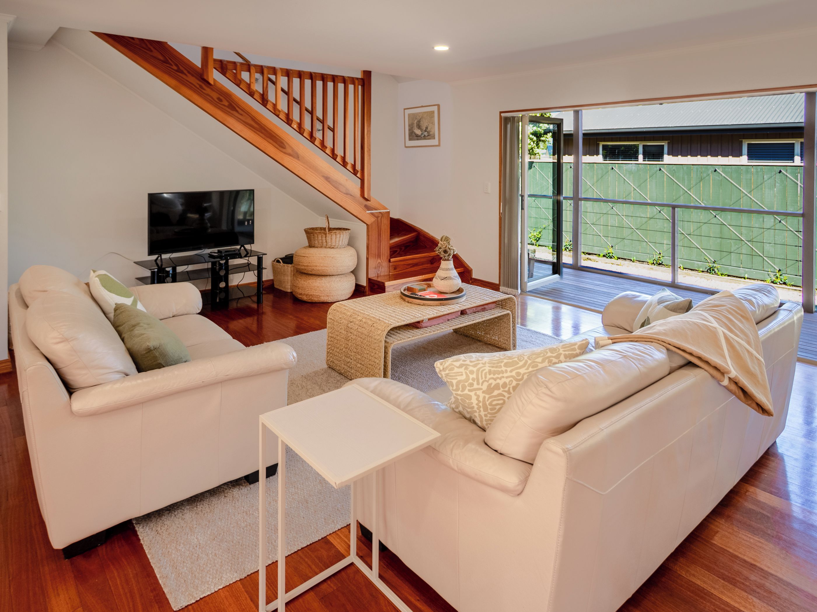 Una sala moderna con una escalera, un televisor de pantalla plana y vistas a un área verde exterior.