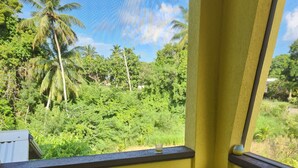 A corner sofa with a view of lush greenery and palm trees. - Matilda Ville – Long-Term 2BR Retreat, The Whim, St. Peter, Barbados. (The Whim)