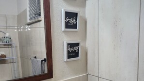 A bathroom with a mirror, three framed signs on the wall, a sink, a soap dispenser, and two glass jars with items. - Matilda Ville – Long-Term 2BR Retreat, The Whim, St. Peter, Barbados. (The Whim)